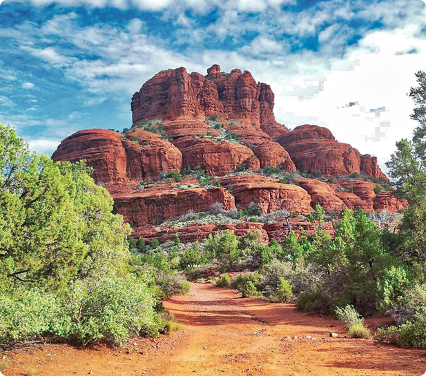 A dirt road leading to a mountain with red rocks.